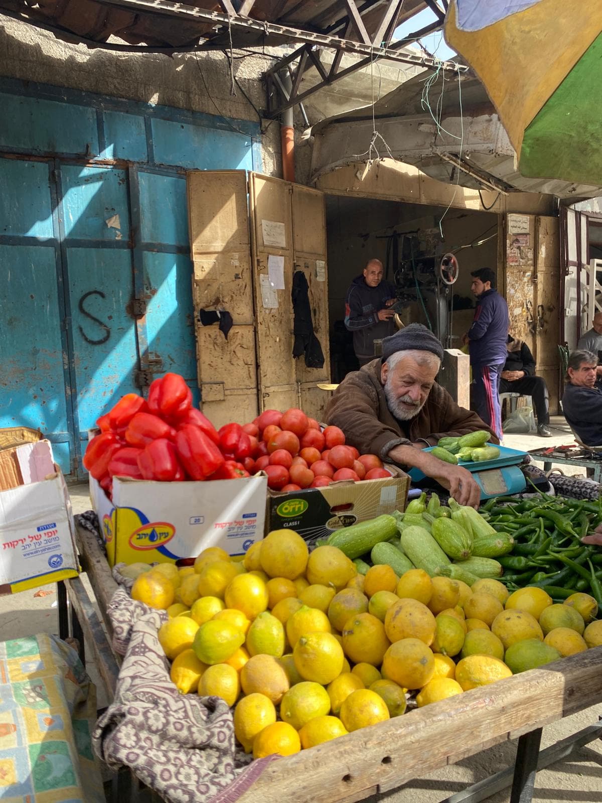 A produce vendor seated among fruit and vegetables at an outdoor market